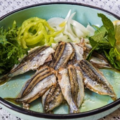 Cooked sardines with green salad in old-fashion plate on table